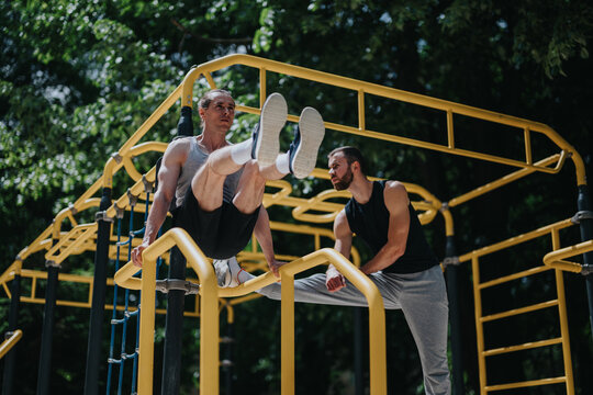 Two athletic men perform a bodyweight L-sit and supported hold on yellow parallel bars during an outdoor workout.