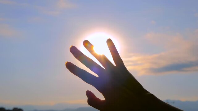 Silhouette of woman is waving her hand against the sunset, sunrise sky, sun is shining through fingers - sun lens flares, close up of moving female arm. Freedom, summer and inspiration concept