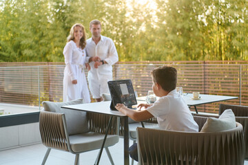 Fototapeta premium Family On Modern Balcony Terrace With Child Using Laptop While Parents Stand In Background