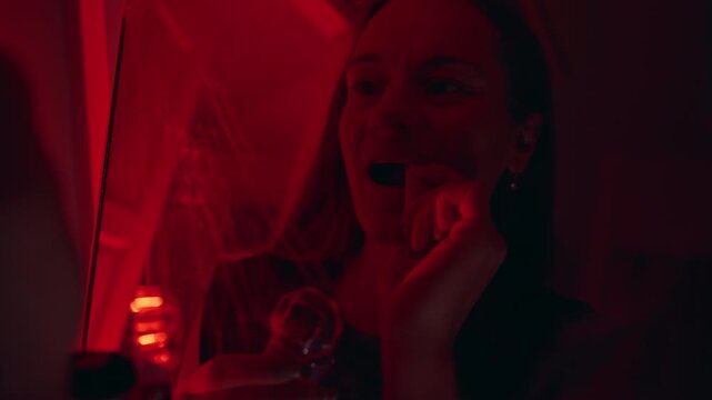 Young Woman Adjusting Artificial Vampire Fangs in Mirror Under Red Light During Halloween Costume Preparation, Horror Character, Spooky Holiday Celebration