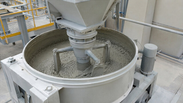 Industrial cement mixer machine blending wet concrete at concrete plant. Automated construction material manufacturing equipment for preparing mortar. Heavy machinery for building industry.