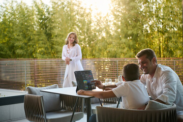 Fototapeta premium Happy Family on Modern Home Balcony Enjoying Sunset Together While Father Shows Son a Tablet