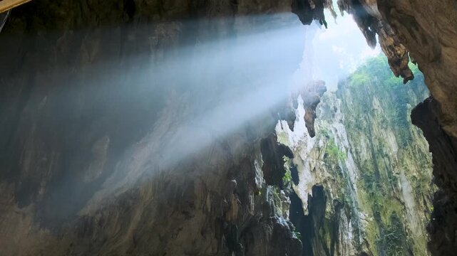 Sunlight streaming in Batu cave entrance, illuminating the rugged rock formations and casting mystical glow, creating serene and mysterious atmosphere, Kuala Lumpur, Malaysia. Hindu travel landmark