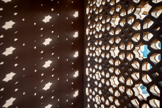 Islamic Geometric Mashrabiya Pattern Casting Sunlight Shadows in Doha, Qatar, Close-up of an intricate Islamic geometric mashrabiya screen casting decorative sunlight and shadow patterns on a wall. 