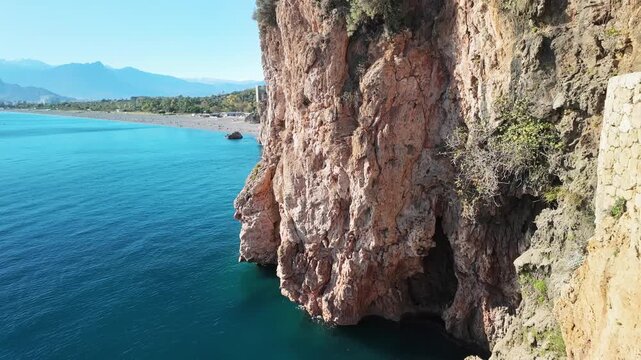 Tilt up shot from turquoise konyaalti sea water to rugged limestone cliff face.