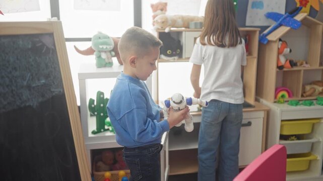 Boy holding white and blue robot toy while crouching beside a wooden play kitchen with girl at sink in a bright playroom building; childlike curiosity.