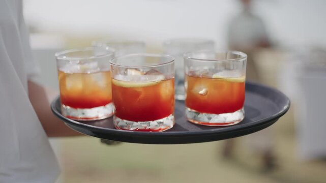 A server carrying a tray of refreshing iced cocktails, featuring vibrant orange layers and citrus garnishes, perfect for summer parties, hospitality, and celebration concepts at a luxury resort.
