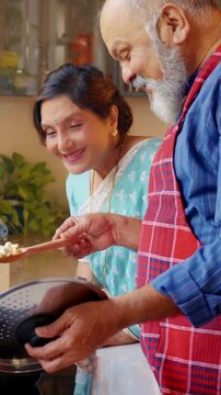 Retired Indian Asian senior couple enjoying their time together in the kitchen, cooking a meal, both relishing the aroma of hot food, sharing moments of joy and warmth