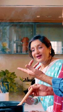 Charming Indian Asian senior couple cooking soup together in their beautiful, well-equipped modern kitchen where husband explains the recipe and wife admires the hot, delicious preparation