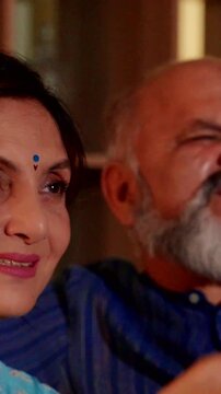 Charming Indian Asian elderly couple relaxing at home, searching for channels on their television together