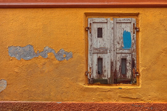 Ground-floor window with dilapidated white wood shutters on the chipped orange facade of a house on Klobovsova ulica street. Skofja Loka-Slovenia-144