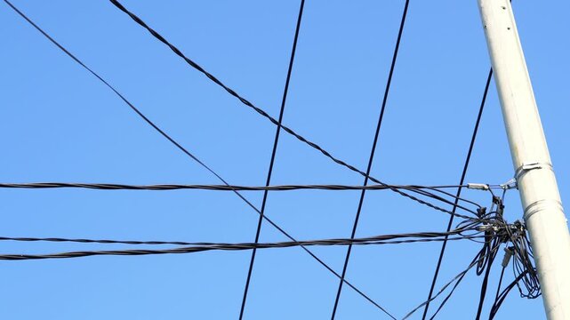 Static footage showing tangled overhead utility wires crossing a bright blue sky. Suitable for urban infrastructure, electricity and city utility concepts.
