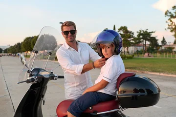 Father Helping Son Fasten Helmet On Scooter During Summer Family Ride In Park © .shock