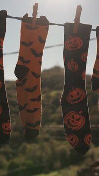 Halloween themed socks with pumpkins and bats hanging on a clothesline outdoors. Spooky and festive laundry drying in the sunlight