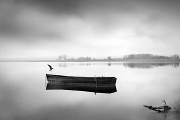 Anchored II rem - A wooden traditional boat at lake Kerkini, anchored to the beach with a bird and a misty, quiert background. © Georgios