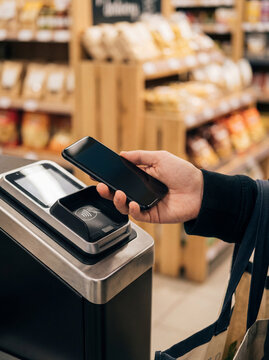 Supermarket checkout mobile wallet payment appears here as an everyday cashless retail action. The smartphone and reader underline digital payment convenience at the counter.