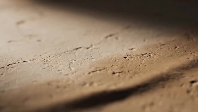 A close-up view of a textured sandy surface with a shadow cast on it