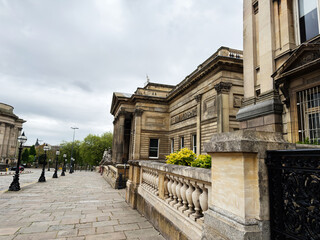Obraz premium Neoclassical civic building with stone columns and balustrade on a wide paved street in Liverpool, UK showing historic architecture and overcast sky