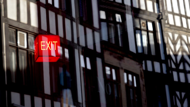 Glowing red exit sign with architectural reflection, escape and emergency concept, double exposure effect with old half timbered building facade