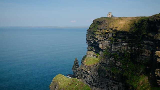Panoramic view of the Cliffs of Moher, Ireland, with O'Brien's Tower standing atop dramatic sea cliffs above the Atlantic Ocean. Stunning coastal landscape featuring rugged rock formations blue waters