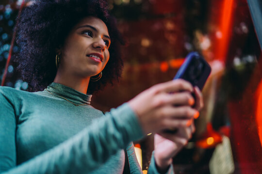 young user checking chat notifications on modern mobile smartphone screen under vibrant red neon glow at night, focused Gen Z person waiting for online instant message feedback outdoors