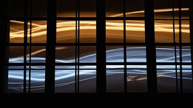 Abstract light trails are visible through a dark window frame at night