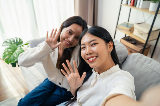 Two young Asian women are taking selfies with smartphone and waving to the camera