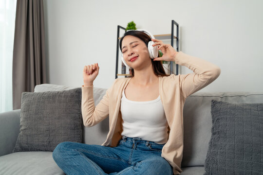 A young Asian woman wearing overear headphones is happily enjoying listening to music.
