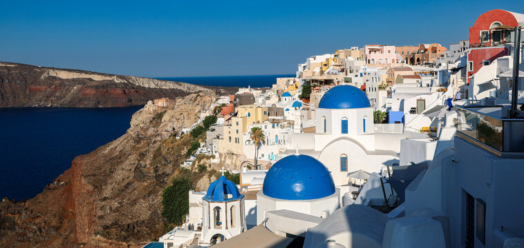 Sunlit view of Oia&rsquo;s iconic blue-domed churches perched above the Aegean Sea, showcasing Santorini&rsquo;s dazzling white architecture, volcanic cliffs, and timeless Mediterranean charm under a clear summer