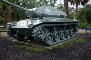 Fototapeta premium A restored historic military tank monument sits on display in a park setting with palm trees and wooden fencing. War Veterans Memorial Park In St. Petersburg, FL conveying military history, remembranc