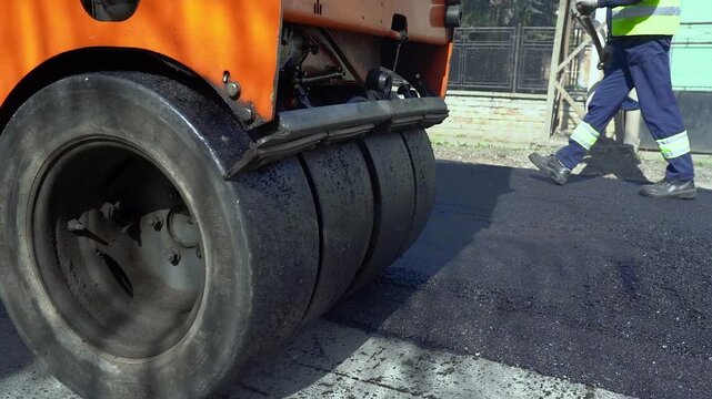 Orange Combination Roller Compacting Hot Asphalt Road Construction Slow Motion. Heavy machinery driving backward on fresh tarmac during city street reconstruction. Great for roadwork concepts.