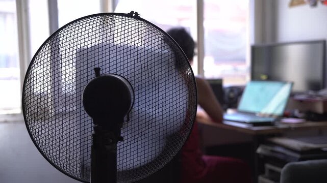 unrecognizable young woman working from home during a hot summer heat wave with fan, cooling off fighting heat during a heatwave and high temperature