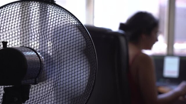 out of focus unrecognizable woman working from home during a hot summer heat wave with fan, cooling off fighting heat during a heatwave and high temperature