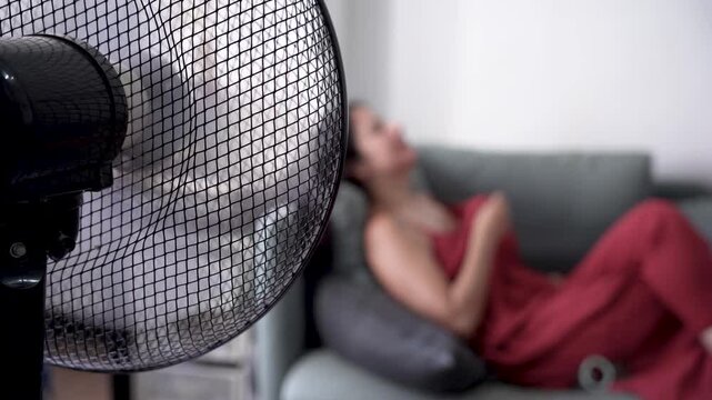 out of focus unrecognizable woman in bed during a hot summer heat wave with fan, cooling off fighting heat at home during a heatwave and high temperature, vertical