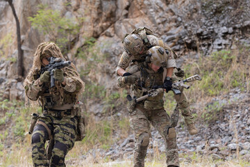 Fototapeta premium Soldier carries injured comrade over rocky terrain