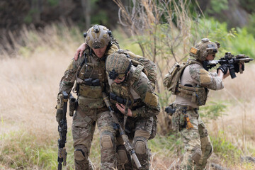 Fototapeta premium Soldier carries injured comrade over rocky terrain