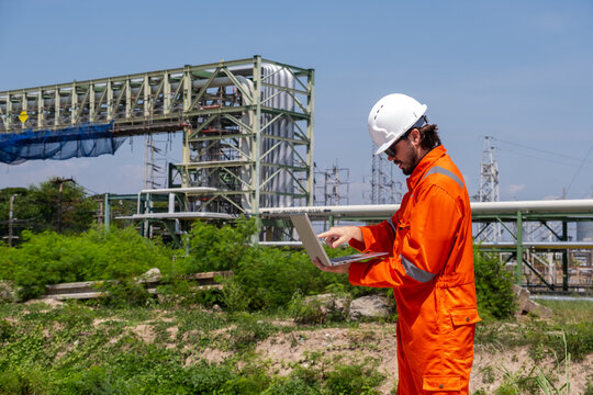 Engineer works on laptop at industrial site during sunny day