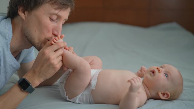 Father kissing little feet of his three month old baby son on bed.