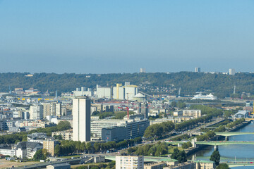 Obraz premium High angle aerial view of Rouen city, featuring modern buildings, industrial port silos, and the Seine river under a clear sky in France. Urban landscape.