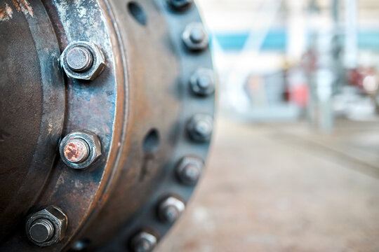 Close-up of industrial machine compressor housing showing sealing connection with bolted screw connection and nuts on manhole at chemical plant with selective focus and blurry background.