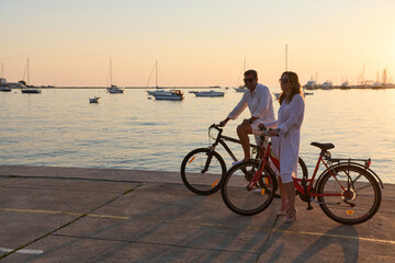 Obraz premium Couple Riding Bicycles Along Marina At Sunset Enjoying Relaxing Seaside Evening Together