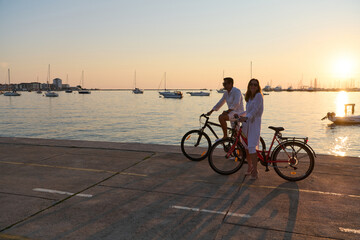 Fototapeta premium Couple Riding Bicycles by the Harbor at Sunset on a Relaxing Seaside Vacation