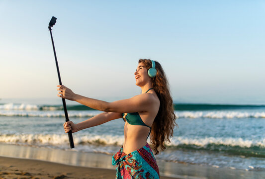 Cheerful young woman creating authentic user generated content while recording herself on a sunny beach, creator lifestyle, personal branding, social media marketing, summer vacation and positive