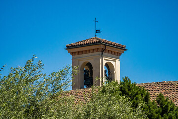 Obraz premium Church Bell Tower with Cross Against Blue Sky Amid Green Trees