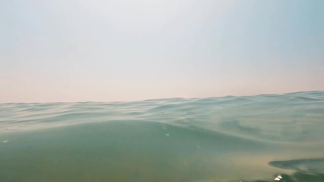 V&iacute;deo grabado a ras de agua en mar abierto, con peque&ntilde;as olas, horizonte bajo y luz solar suave sobre la superficie. La escena tiene una est&eacute;tica minimalista y serena, con tonos turquesa y una sensaci