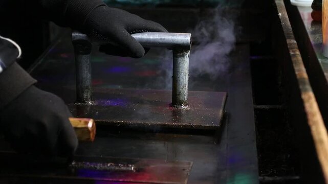 Gloved hand holding metal handle over hot griddle steam rising closeup of cooking tool and surface with grilled squid