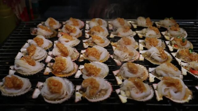 Grilled scallop shell with glass noodles, garlic butter and savory sauce on street food grill. steamy, appetizing noodle and garlic seafood delight