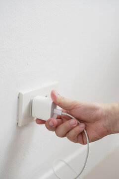 close up hand plugging adapter charge the battery with outlet socket plug and hold mobile phone on wall ,electric safety concept