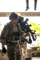 Fototapeta premium Male soldier in fully combat tactical military uniform and holding automatic war rifle, cautiously conducting a patrol and security sweep inside a ruined abandoned building