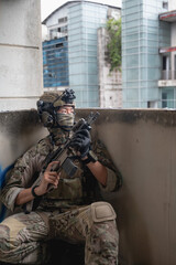 Fototapeta premium Male soldier in full military tactical uniform and combat gear hiding behind a wall, preparing for ambush attack with his weapon ready inside a dark ruined abandoned building